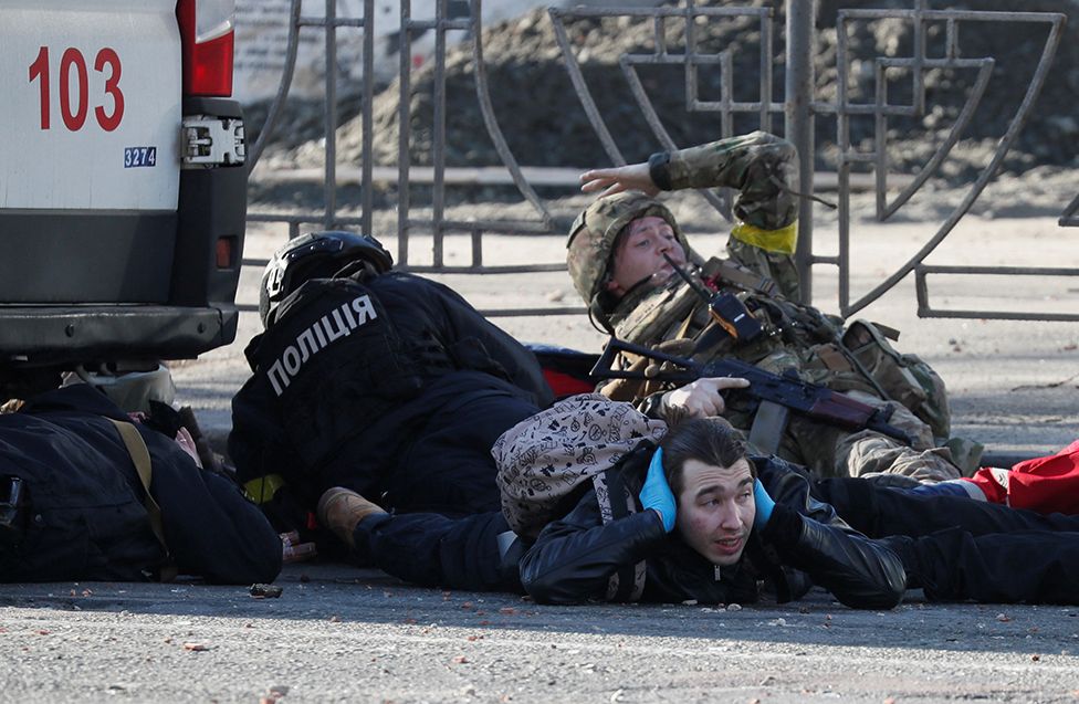 People take cover as an air-raid siren sounds, near an apartment building damaged by recent shelling in Kyiv, Ukraine February 26, 2022.