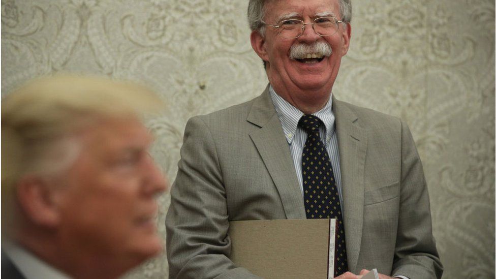 President Donald Trump speaks to members of the media as National Security Adviser John Bolton listens during a meeting with President of Romania Klaus Iohannis in the Oval Office of the White House August 20, 2019