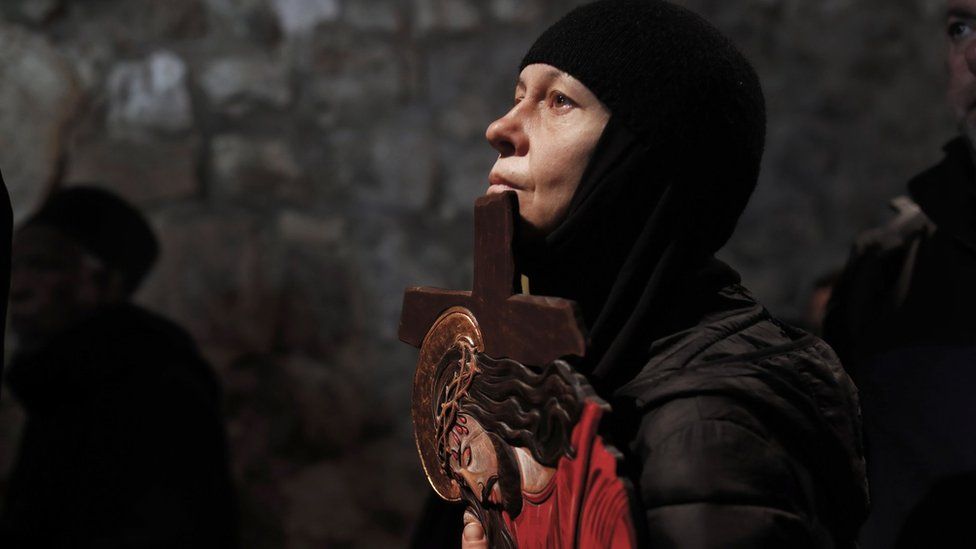 A Christian Orthodox pilgrim holds a cross with a depiction of Jesus