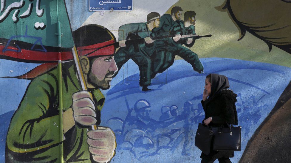 An Iranian woman walks past a mural in Tehran, 16 January
