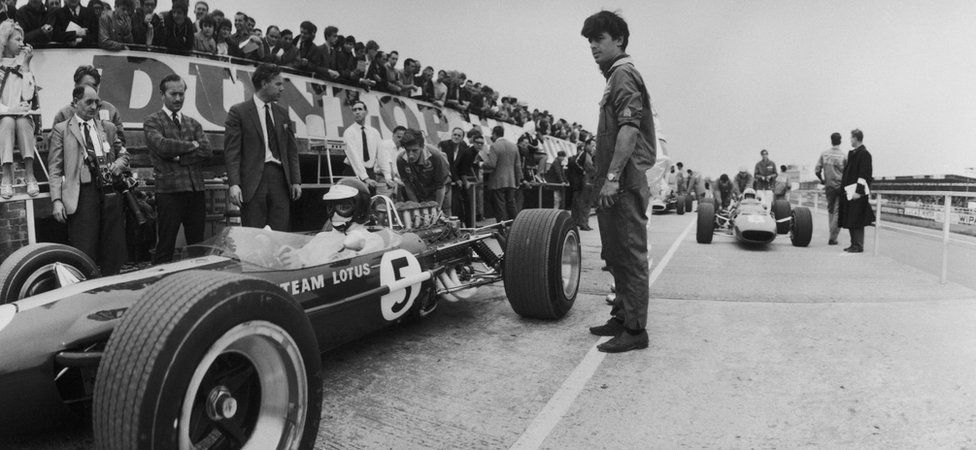Jim Clark (pictured left in his Lotus car) , his fifth British Grand Prix win and his last. Lotus boss Colin Chapman looks on with arms folded (left)