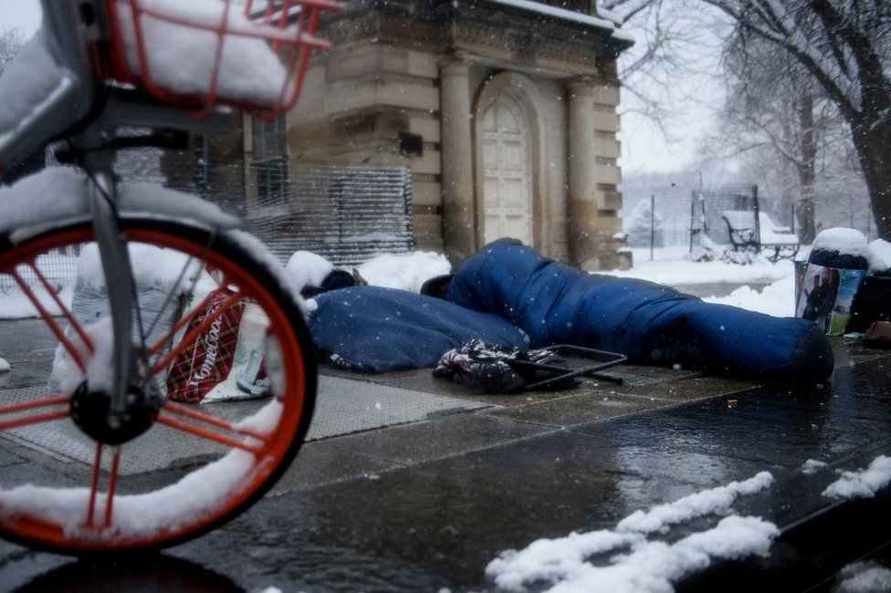 A man in a sleeping bag sleeps in the snow