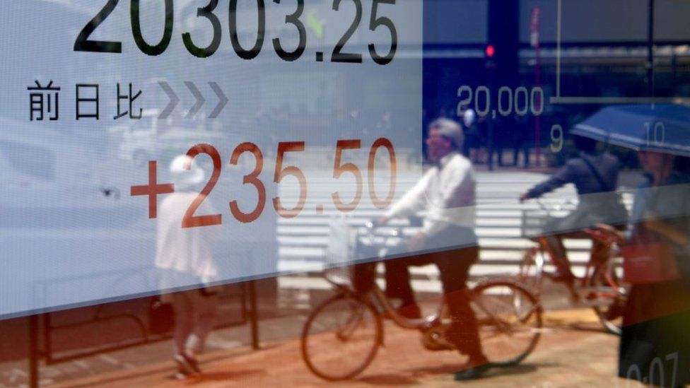 Pedestrians are reflected in the window of a securities company displaying the numbers on the Tokyo Stock Exchange along a street in Tokyo