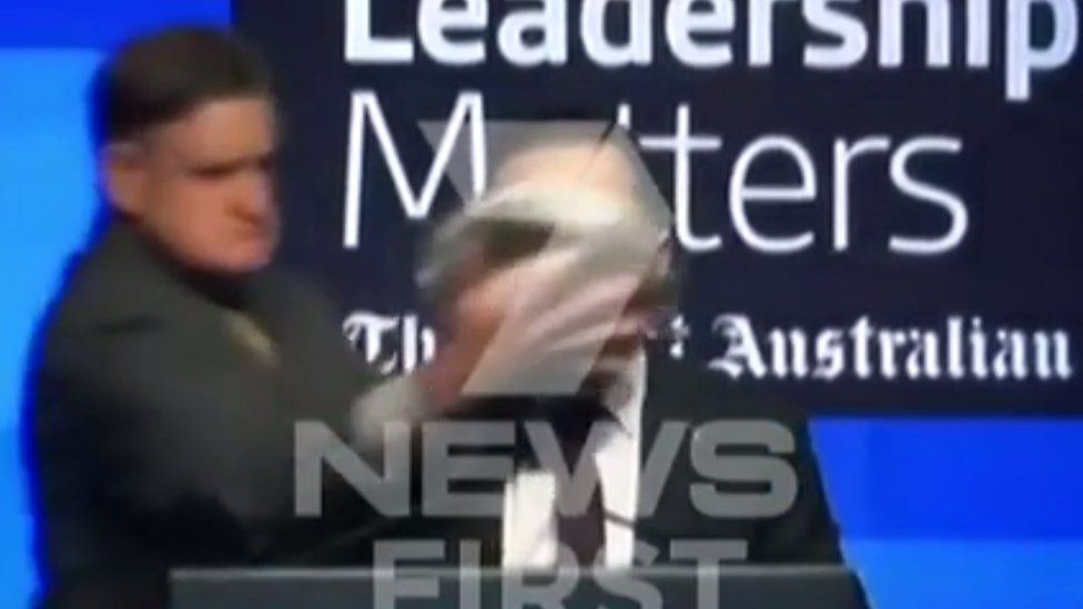 The assailant attacks Alan Joyce with a pie