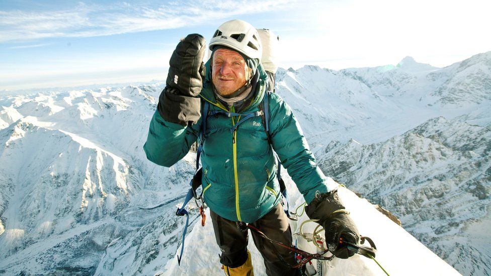 Tomasz Mackiewicz, wearing a green climbing coat, is pictured on top of a snow-white mountain range