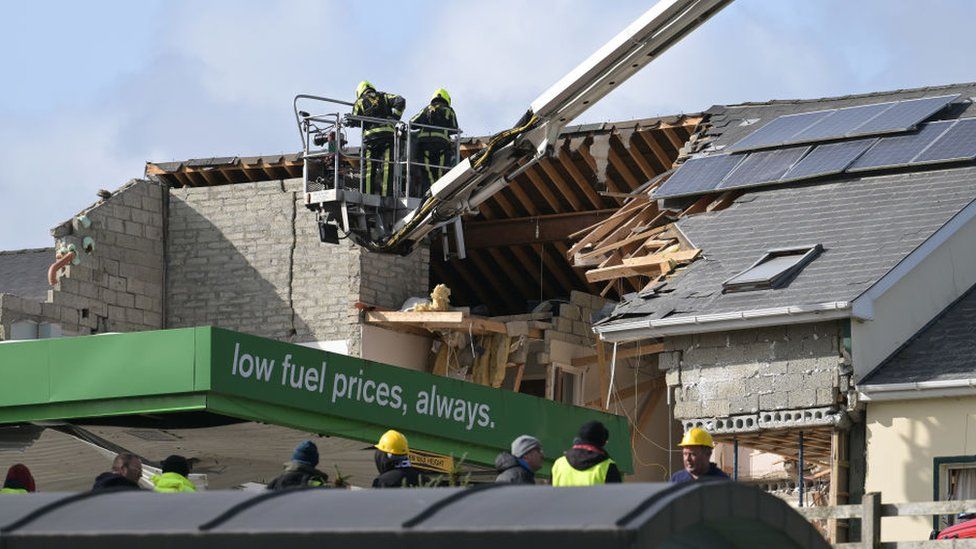 Firefighters on a mechanical platform assess the damage caused to the service station and a nearby apartment block