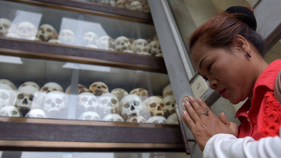 A woman prays in front of skulls of Khmer Rouge victims at the Killing Fields