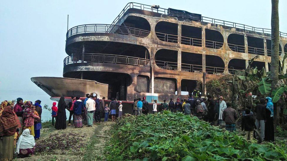 Villagers look at a burnt-out ferry after it caught on fire killing at least 30 people in Jhakakathi, 250 kilometres (160 miles) south of Dhaka, 24 December 2021