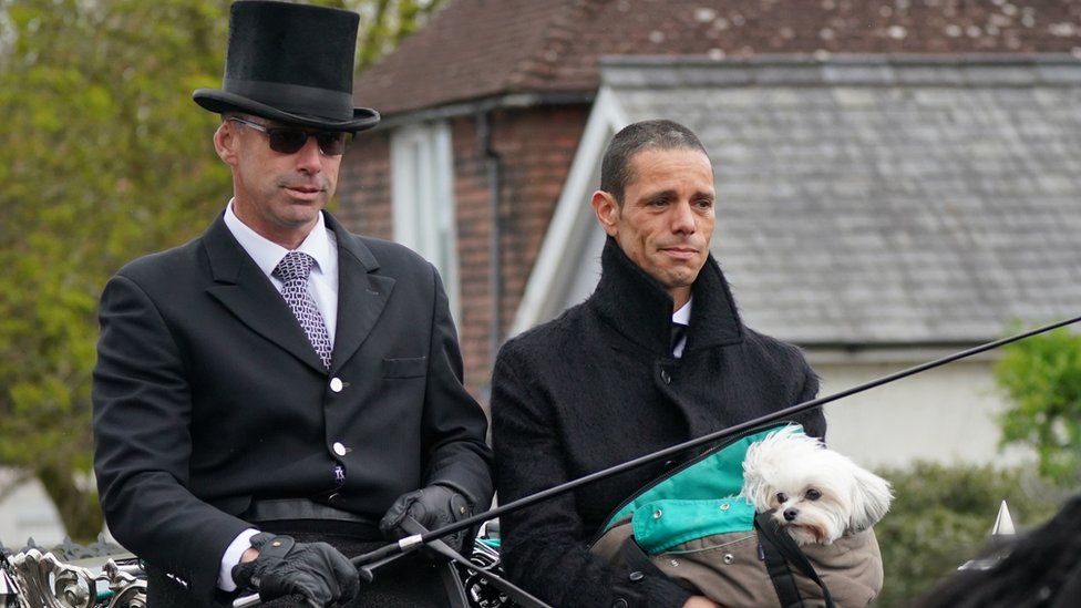Husband of Paul O'Grady Andre Portasio (right)rides with the funeral cortege as it travels through the village of Aldington