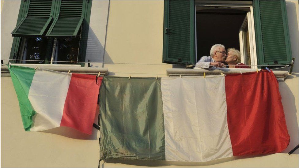 A couple kiss at the window of their home from which flags are displayed during the lockdown in Italy