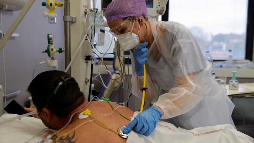 A doctor wearing a protective suit and a face mask, examines a patient in the intensive care unit in France