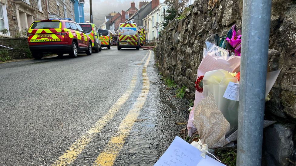 Floral tributes and emergency vehicles at fire scene