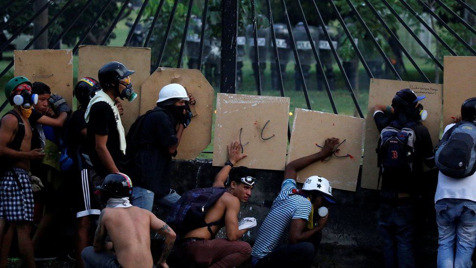 The military (in the background) take position at a Caracas air base as opposition supporters rally