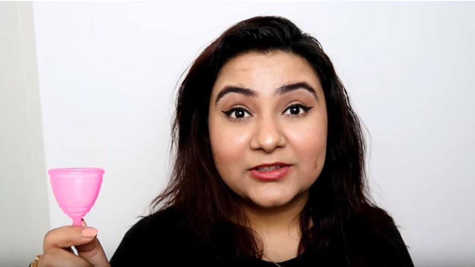 Komal holds up a pink plastic menstrual cup in a YouTube grab