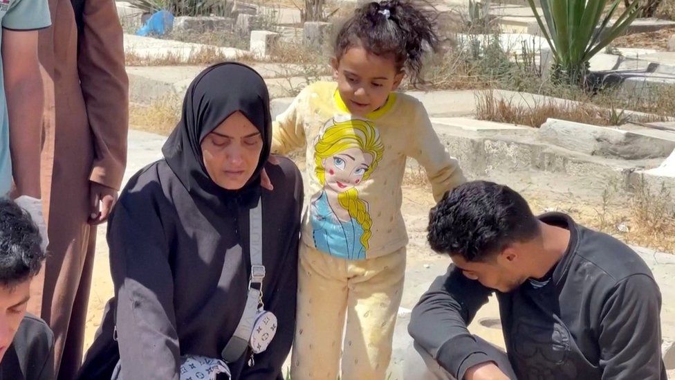 Somaya al-Shourbagy (left) kneels next to her husband's grave, as their daughter Hind (centre) stands alongside her at a cemetery in Khan Younis, in the southern Gaza Strip (24 April 2024)