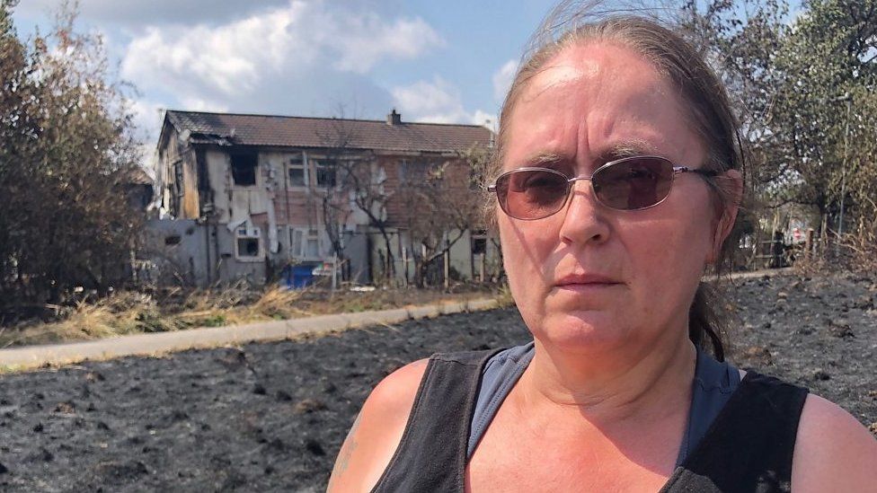 Woman stands infront of burnt out house