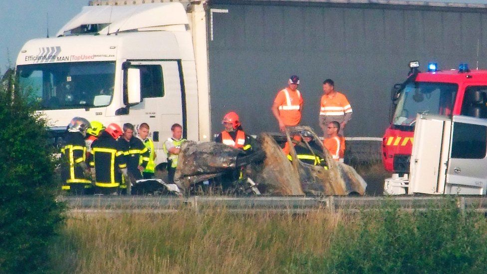 Firefighters and rescuers stand next to the wreckage of a van after it collided with a barricade made with tree trunks set up by migrants on the A16 highway near Guemps, northern France, on 20 June
