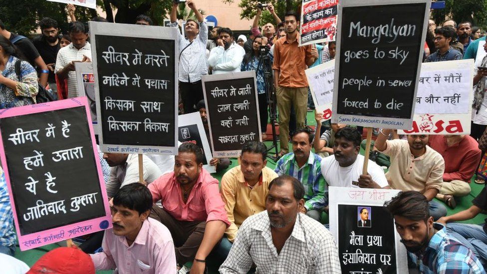 NEW DELHI, INDIA - SEPTEMBER 25: People hold placards during a protest against the violation of Manual Scavenging Prohibition Act 2013, at Jantar Mantar, on September 25, 2018 in New Delhi, India. Protestors display a photo of BR Ambedkar in front of a banner displaying photos of manual scavengers who lost their lives, during a protest. (Photo by Sushil Kumar/Hindustan Times via Getty Images)