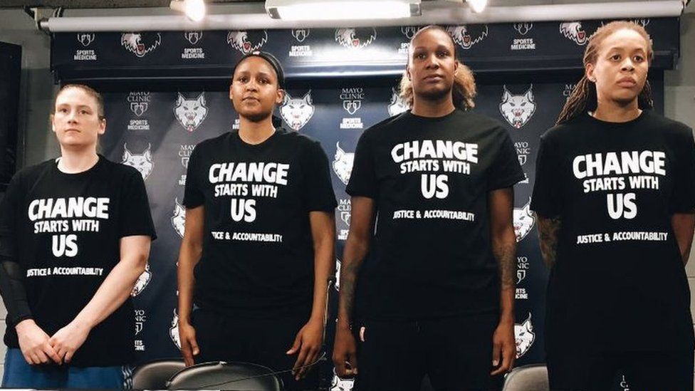 Maya Moore, Seimone Augustus, Lindsay Whalen, and Rebekkah Brunson wearing black shirts with the phrase “Change Starts With Us: Justice & Accountability.”