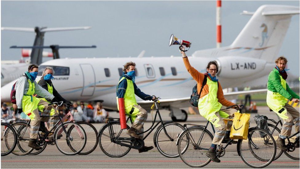Demonstrators on bicycles in front of a private jet at Schiphol Airport on 5 November
