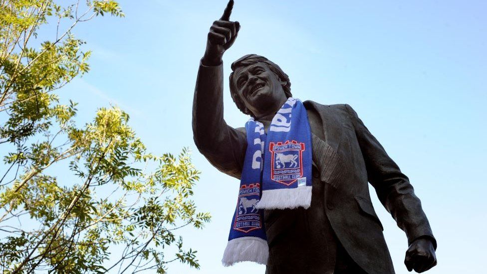 Sir Bobby statue with an Ipswich Town scarf outside Portman Road