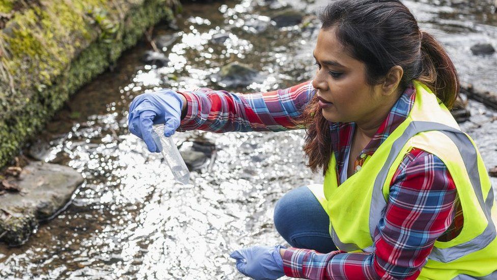 A female scientist holds up a test tube with a water sample from a stream in Hexham and is analyzing the sample for traces of pollutants and also for traces of small microplastics