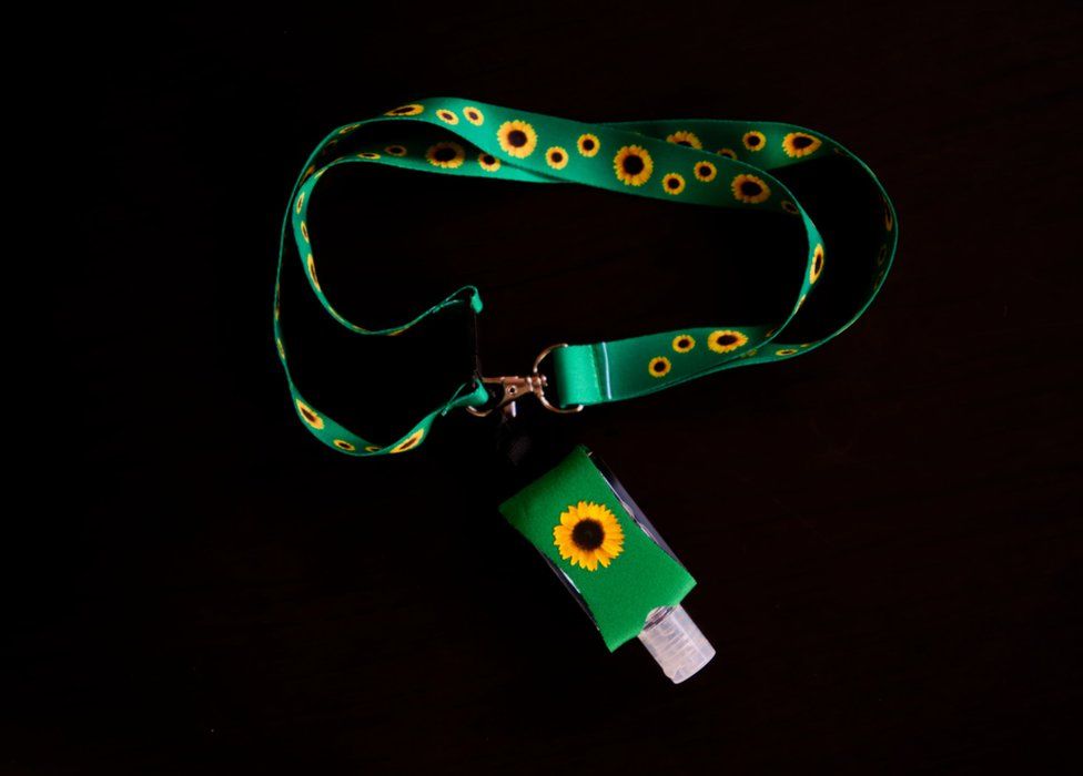 A green and yellow lanyard with sunflower motif which denoted a hidden disability. This lanyard also has a small hand sanitiser bottle held in a neoprene sleeve
