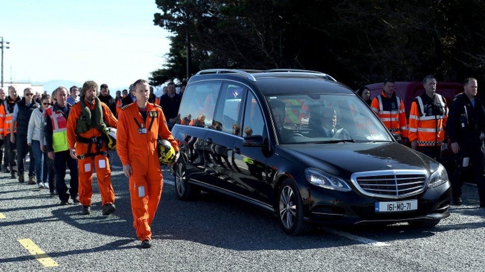 The body of Captain Mark Duffy is driven in a hearse accompanied by a guard of honour