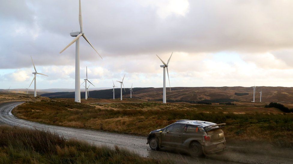 A car drives in front of wind turbines in Newtown, Powys