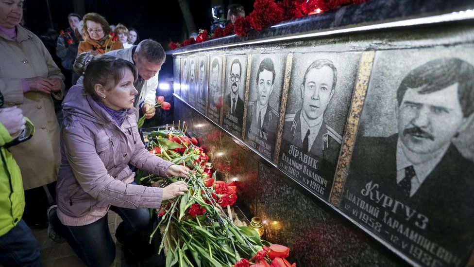 A woman lays flowers at a memorial, dedicated to firefighters and workers who died after the Chernobyl nuclear disaster, during a night service in the city of Slavutych, Ukraine, April 26, 2016.