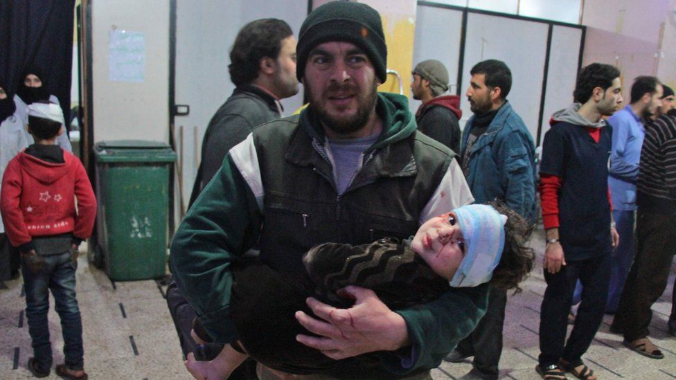 A Syrian man carries a wounded infant at a makeshift hospital in the rebel-held town of Douma, 20 February 2018