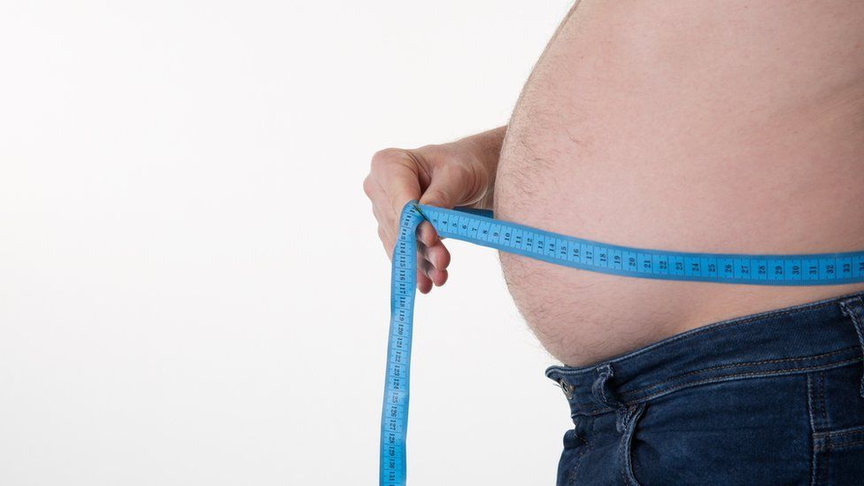 An overweight man with a tape measure around his tummy