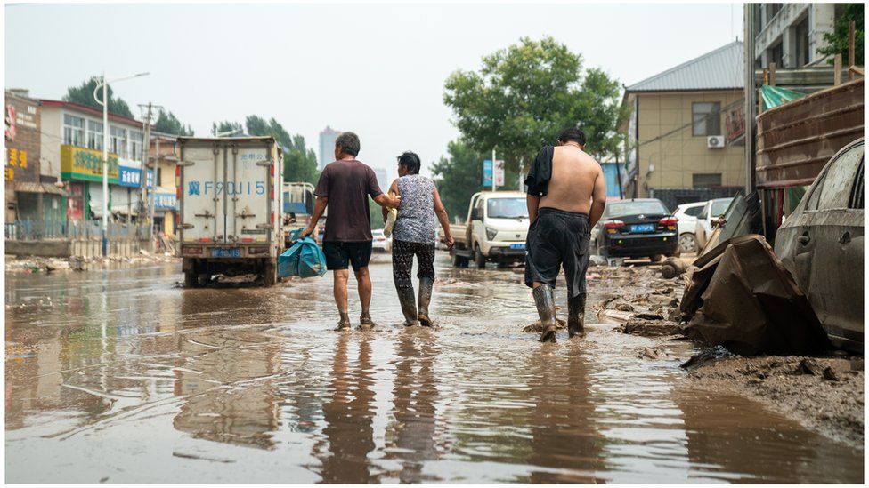 Three people walk down a flooded street in Zhuozhou