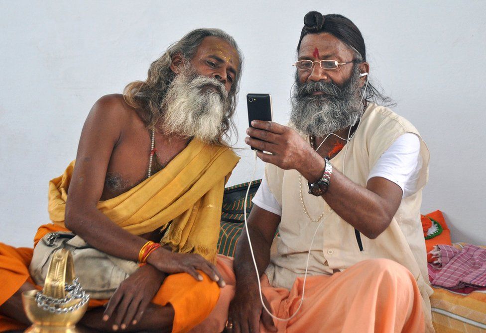 Hindu holy men look at a mobile phone as at a temple