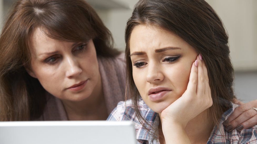 Mother comforting daughter near laptop