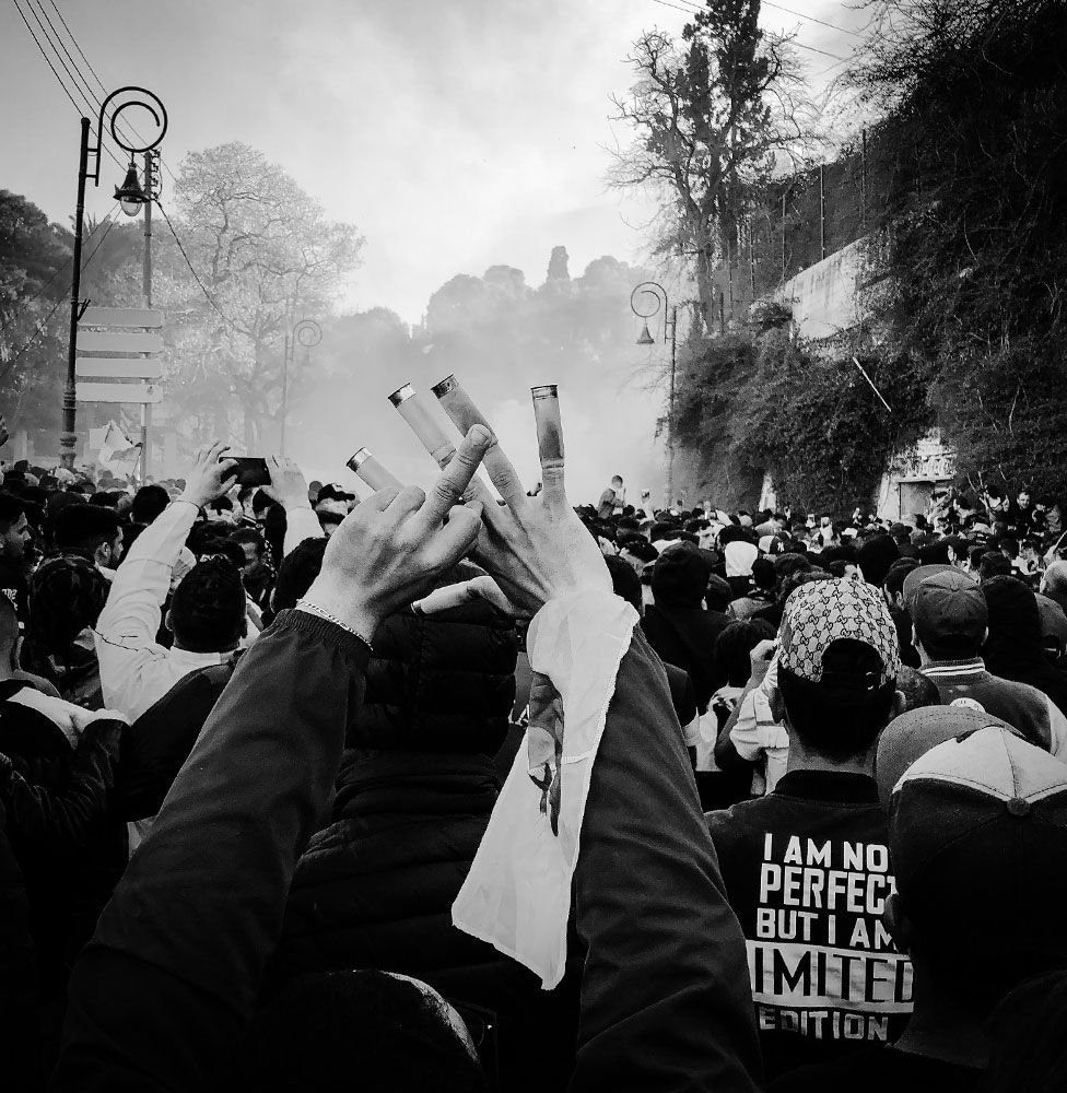 A protester shows the middle finger with one hand and has five empty tear gas cartridges in the fingers of his other hand