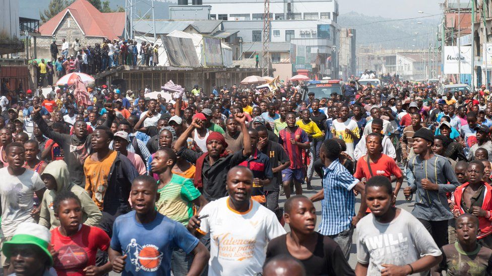 Civilians cheer as they escort a military ambulance carrying the body of a Congolese soldier shot dead in Rwanda