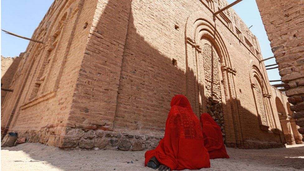 Two woman praying at a shrine. They are dressed in red.