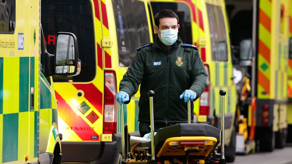 A paramedic wearing a face mask pushes a stretcher past ambulances parked outside the emergency department of the Royal London Hospital in London, on 11 January 2021