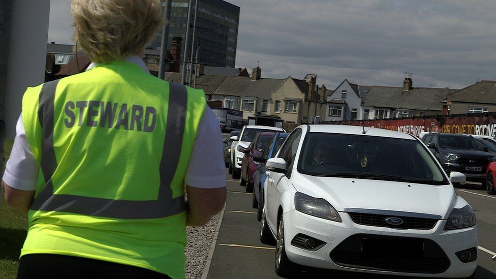 Steward guides a queue of cars at Rodney Parade