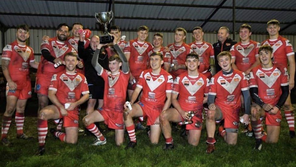 Cameron holds a trophy up surrounded by smiling teammates