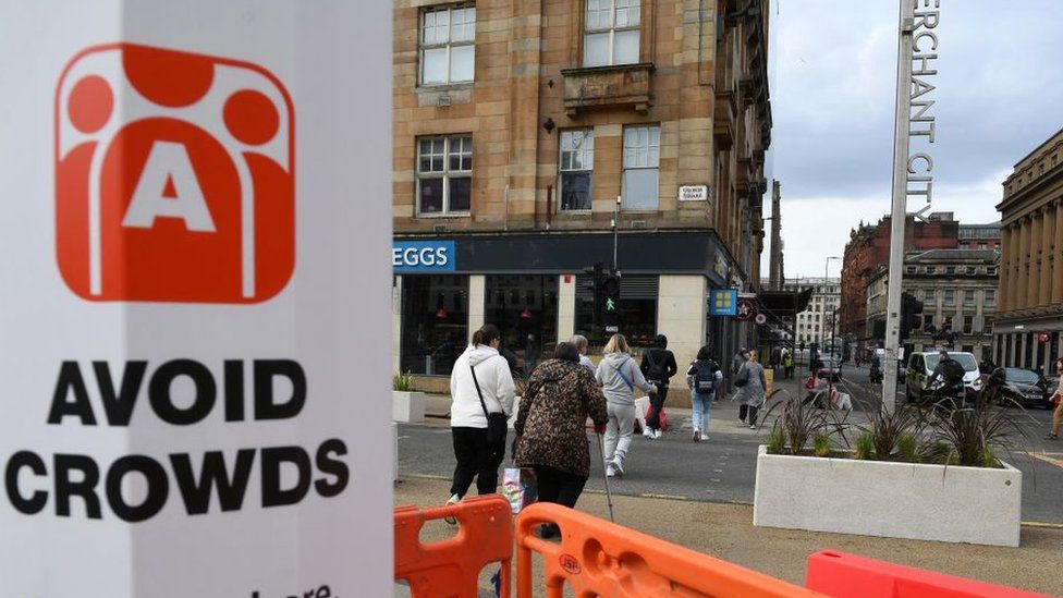 A sign alerts pedestrians and shoppers to "Avoid Crowds" due to Covid-19 in Glasgow
