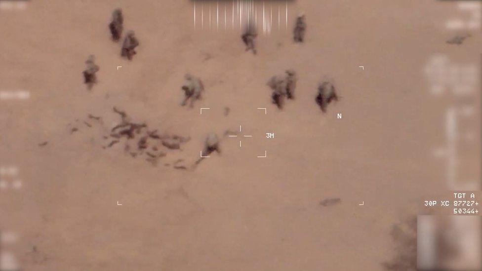 Screengrab of drone footage showing two people throwing sand over the bodies