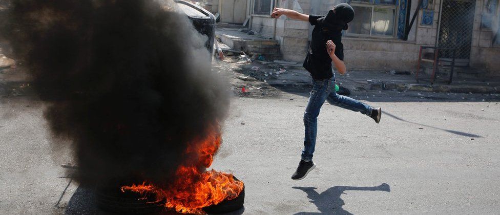 A masked Palestinian protester throws a stone at Israeli troops at the Qalandia checkpoint, 22 May