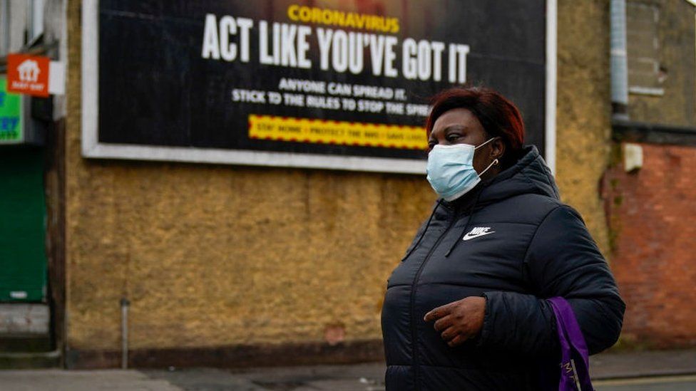 A pedestrian wearing a face covering walks past a coronavirus information poster in Manchester in February 2020