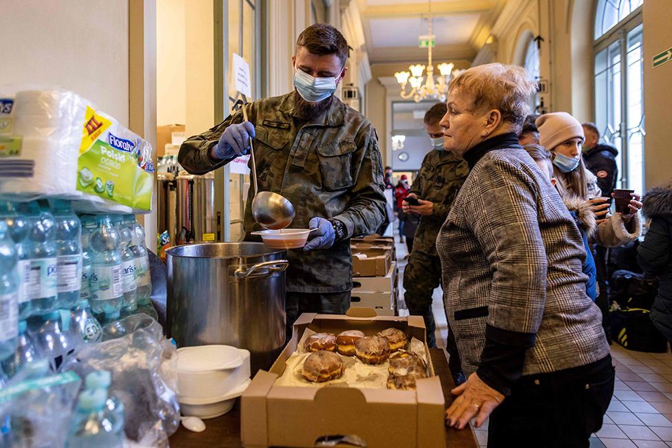 A soldier serves soup to a Ukrainian woman in the building of the main railway station of Przemysl which has been turned into a temporary reception centre for refugees