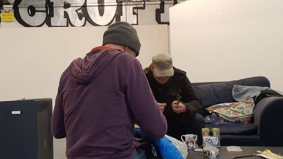 Two men sewing labels onto blankets for homeless people