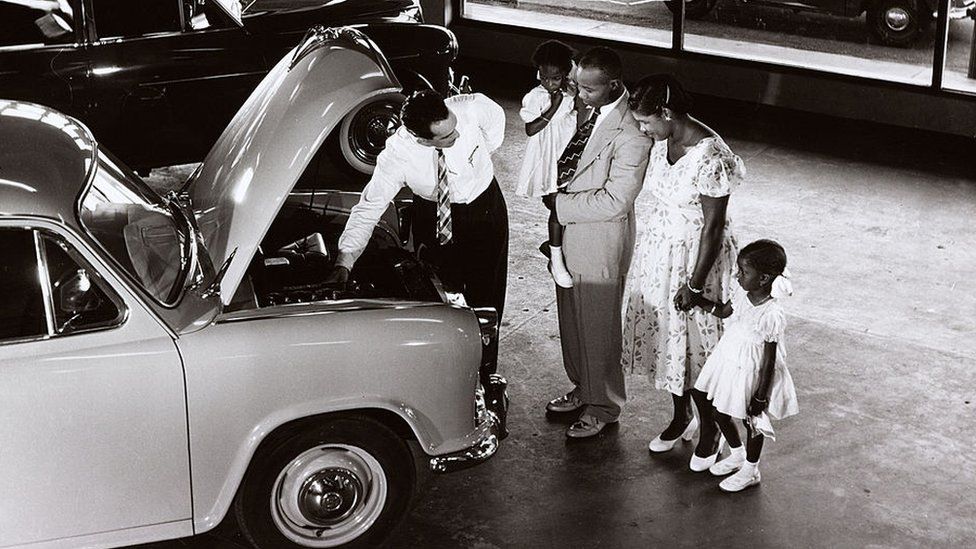A family in Guyana are shown a Morris car in a showroom, 1958.