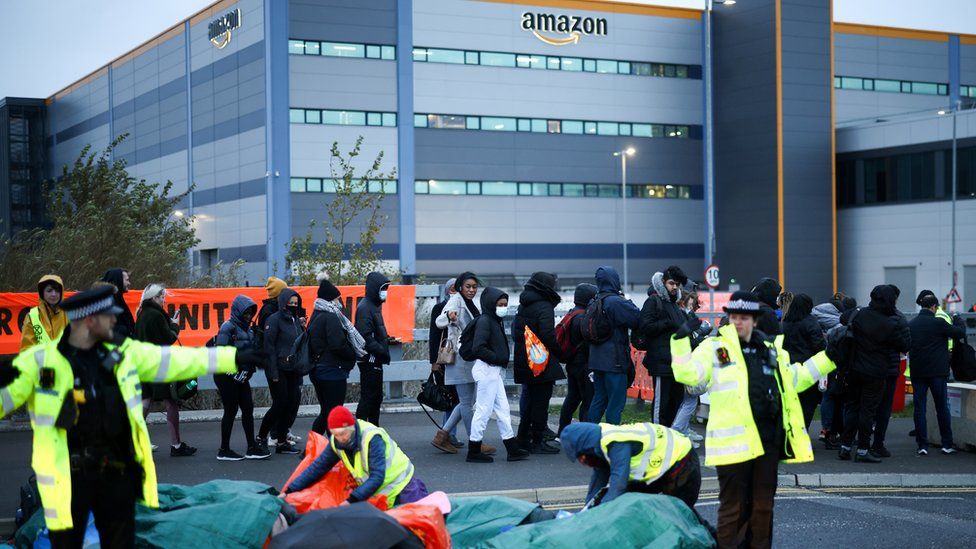 A line of Amazon workers walks past protesters and police in high-viz vests