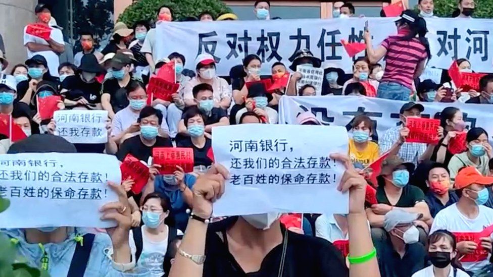 Protestors hold up signs outside a People's Bank of China building in Zhengzhou in the Henan province on Sunday.